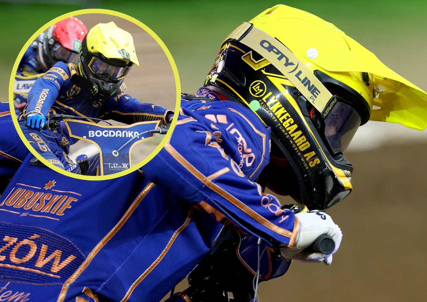 Zawodnik żużlowy w niebieskim kombinezonie i żółtym kasku podczas wyścigu, zbliżenie na twarz z widocznymi nazwami sponsorów, w tle inny motocyklista.