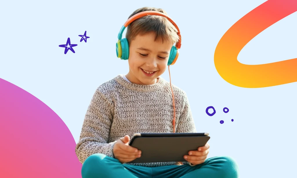 Chłopiec w kolorowych słuchawkach, uśmiechnięty, siedzi i korzysta z tabletu na tle graficznych, kolorowych elementów.