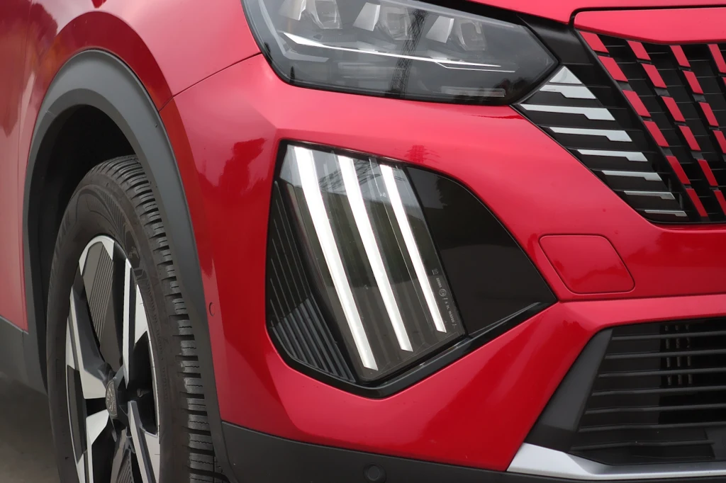Charakterystyczne światła to znak rozpoznawczy aut po liftingu Czerwony samochód, zbliżenie na nowoczesny reflektor LED oraz fragment błotnika z widocznym elementem felgi aluminiowej.