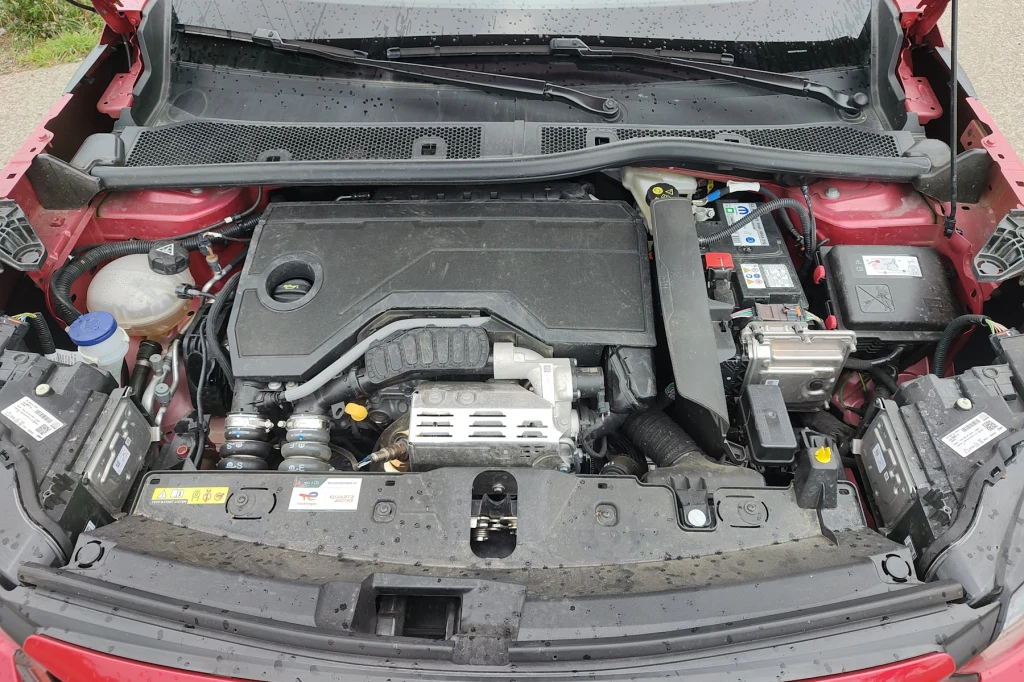 Hybrydowy napęd Peugoeta 2008 składa się z silnika 1.2 o mocy 136 KM i silnika elektrycznego generującego 28,5 KM Silnik samochodu osobowego z widocznymi elementami takimi jak akumulator, zbiornik płynu chłodniczego, przewody i obudowa silnika, całość zamontowana w czerwonym nadwoziu auta.