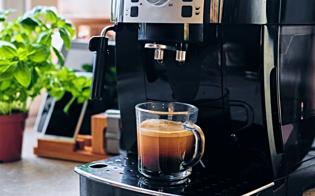 Masz w domu to urządzenie? Uważaj, może rujnować budżet Ekspres do kawy podczas przygotowywania kawy do przezroczystej szklanki. W tle widoczna zielona roślina doniczkowa oraz kuchenne akcesoria.