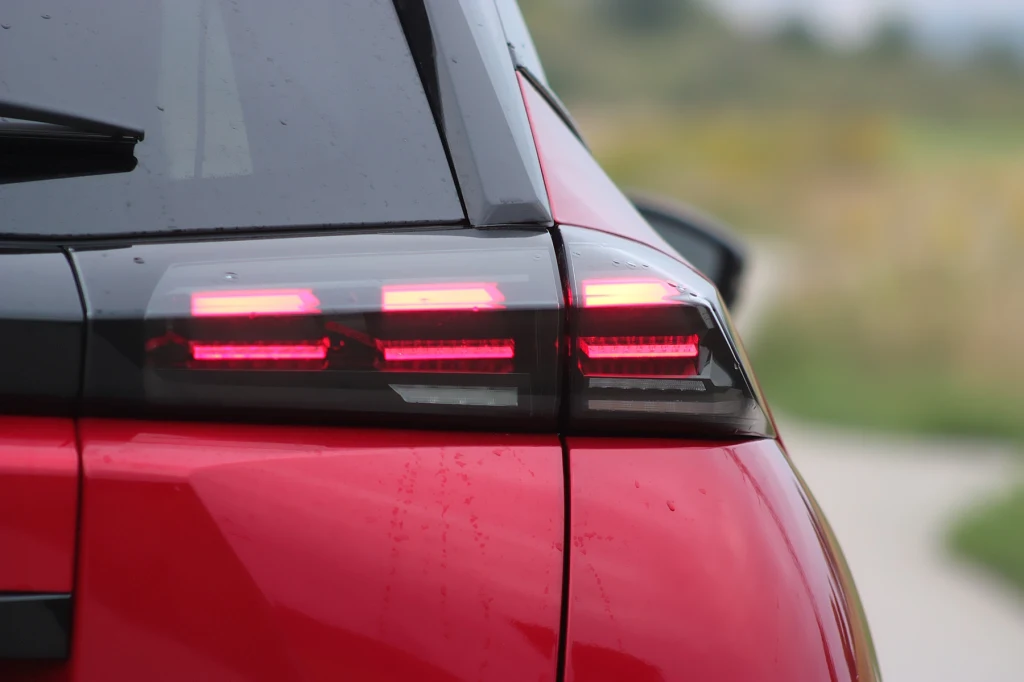 Potrójne światła tylne to również nowość, która pojawiła się w samochodach po liftingu Tylna lampa nowoczesnego czerwonego samochodu z zapalonymi światłami, na rozmytym tle wiejskiej drogi.