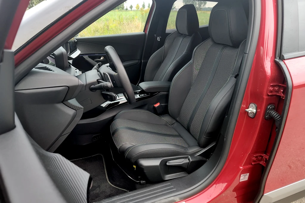 Przednie fotele są wygodne i zapewniają dobre trzymanie boczne. Elektryczna regulacja tylko w opcji Wnętrze nowoczesnego samochodu osobowego z widocznymi przednimi fotelami w czarnym kolorze, otwartymi drzwiami kierowcy oraz minimalistyczną deską rozdzielczą i panelem sterowania.