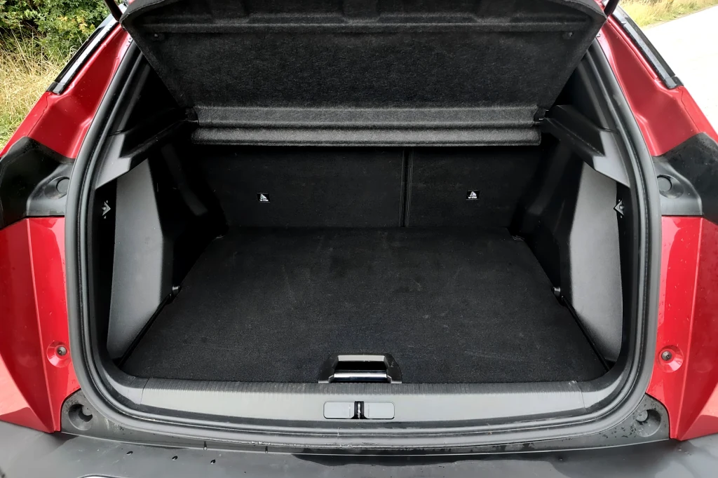 Bagażnik ma 430 litrów pojemności, jak na segment B to świetny wynik Otwarty bagażnik czerwonego samochodu, wyłożony czarną wykładziną, bez żadnych przedmiotów w środku. W tle widoczna część zieleni i asfaltowej drogi.
