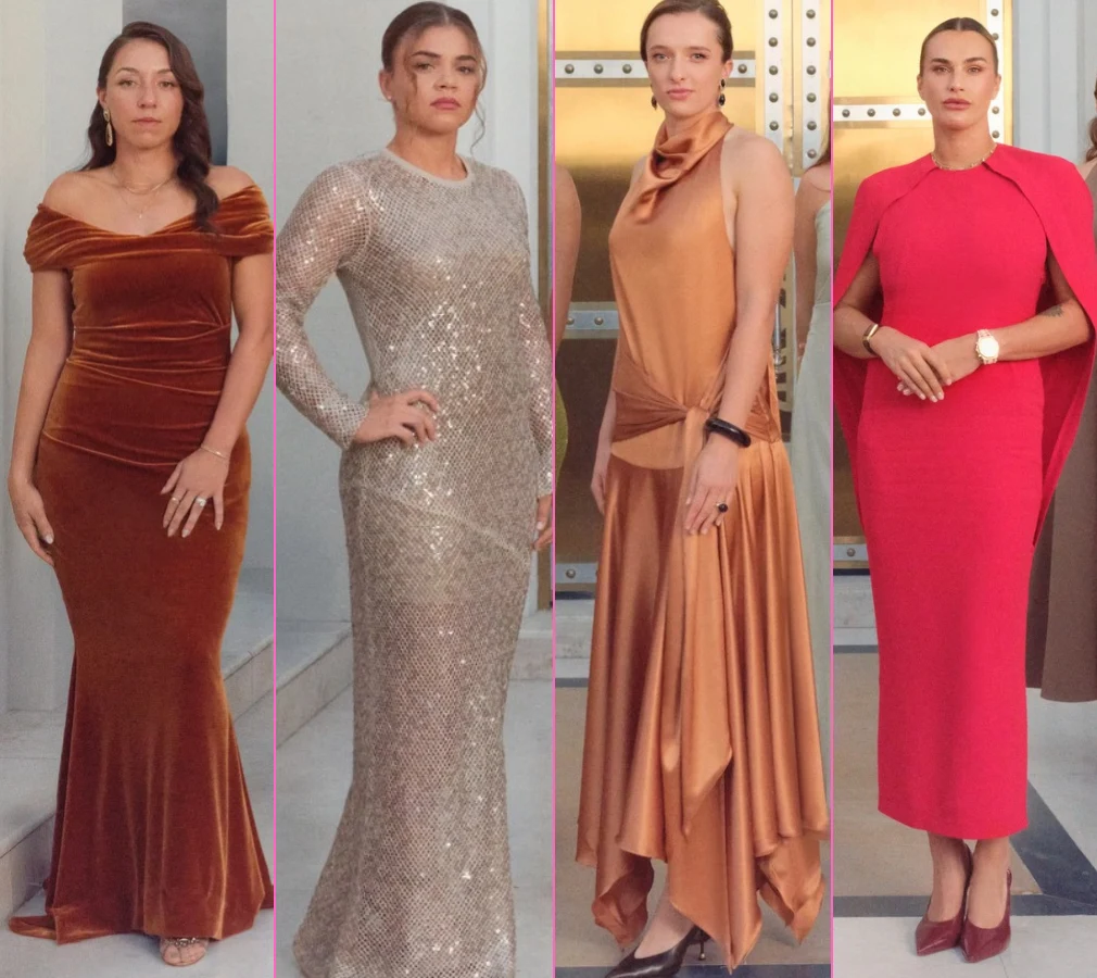 Cztery kobiety stoją w rzędzie, każda ubrana w elegancką suknię wieczorową w różnych stylach i kolorach. Tło stanowi luksusowe wnętrze z metalowymi drzwiami.