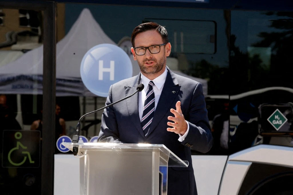 Daniel Obajtek zostanie przesłuchany przez prokuraturę Mężczyzna w garniturze przemawia na tle autobusu z symbolem wodoru H, używa mównicy z mikrofonem; widoczne symbole dostępności oraz oznaczenia ekologiczne.