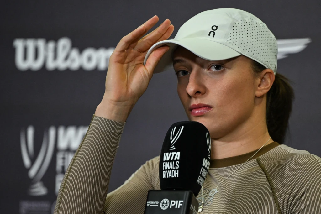 Tenisistka w jasnej czapce i sportowym stroju siedzi przy mikrofonie podczas konferencji prasowej, w tle widać logo związane z finałami WTA w Rijadzie.