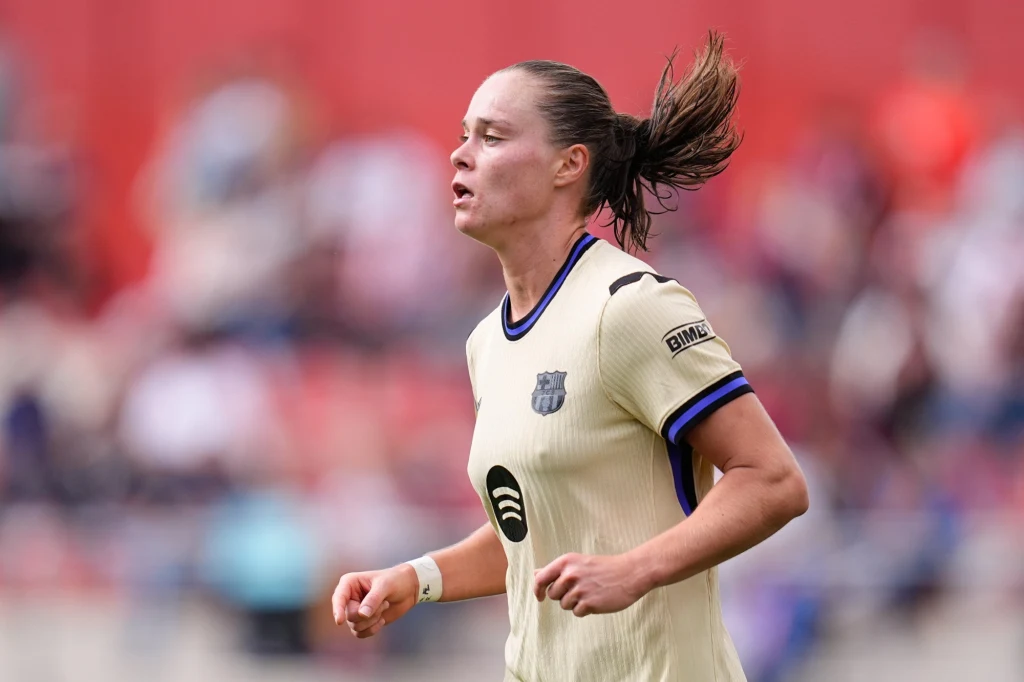 Ewa Pajor Piłkarka w kremowej koszulce z herbem FC Barcelona podczas meczu, skupiona w trakcie biegu, w tle rozmazana publiczność na stadionie.