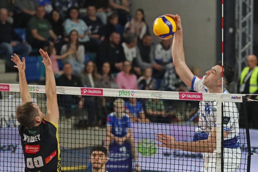 W ataku Asparuh Asparuhow Dwóch siatkarzy w trakcie akcji przy siatce, jeden z nich wykonuje atak, drugi próbuje zablokować piłkę. W tle widoczna publiczność oraz pozostali zawodnicy.