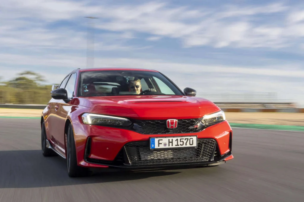 Czerwony samochód Honda porusza się dynamicznie po torze wyścigowym, kierowany przez mężczyznę, tło rozmazane wskutek ruchu