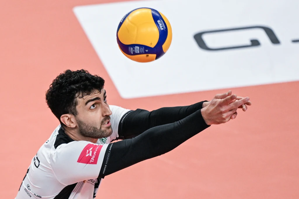 Marcin Janusz, nowy rozgrywający Asseco Resovii Siatkarz wykonujący odbiór piłki podczas meczu, skupiony na precyzyjnym podaniu, z jasno widoczną siatkarską piłką lecącą w jego kierunku i charakterystycznym sportowym strojem