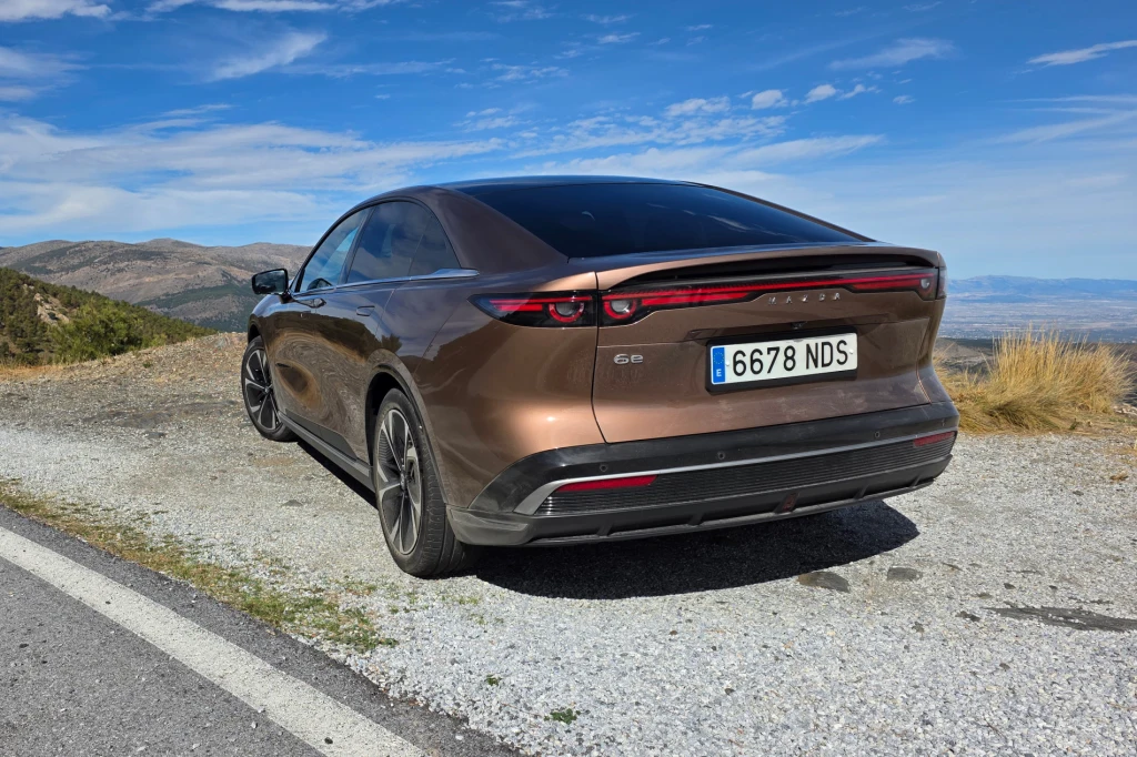 Mimo wyglądu sedana 6e jest tak naprawdę liftbackiem - pokrywa bagażnika otwiera się w niej wraz z szybą Brązowy, nowoczesny samochód elektryczny zaparkowany przy górskiej drodze, z widokiem na rozległy krajobraz, jasne niebo z lekkim zachmurzeniem i tablica rejestracyjna widoczna z tyłu pojazdu.