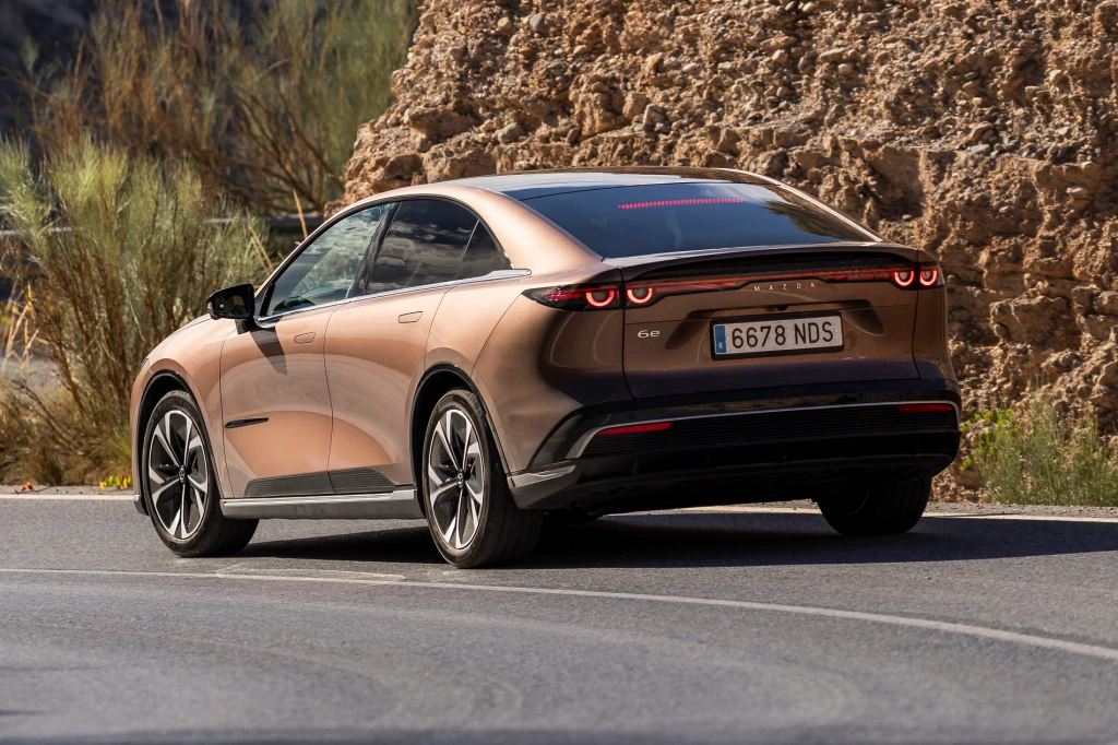 Szerokie słupki i mocno pochylona szyba nie wpływają dobrze na widoczność z wnętrza. Dobrze, że obraz z kamer jest wysokiej jakości Brązowy samochód osobowy o nowoczesnej sylwetce, zaparkowany na asfaltowej drodze przy skalistej ścianie. Pojazd wyróżniają charakterystyczne, poziome tylne światła LED oraz elegancka linia nadwozia typu fastback.