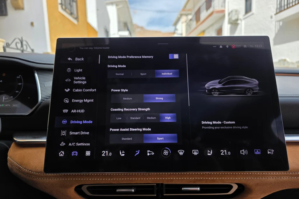 Można wybierać spośród trzech trybów jazdy (Normalnym, Sportowy i Indywidualny), w tym ostatnim dostępne są cztery poziomy odzysku energii Wnętrze samochodu z wyeksponowanym dużym ekranem dotykowym, na którym widoczny jest interfejs sterowania trybami jazdy, komfortem kabiny, zarządzaniem energią oraz innymi funkcjami pojazdu, w tle fragmenty deski rozdzielczej i kierownicy.
