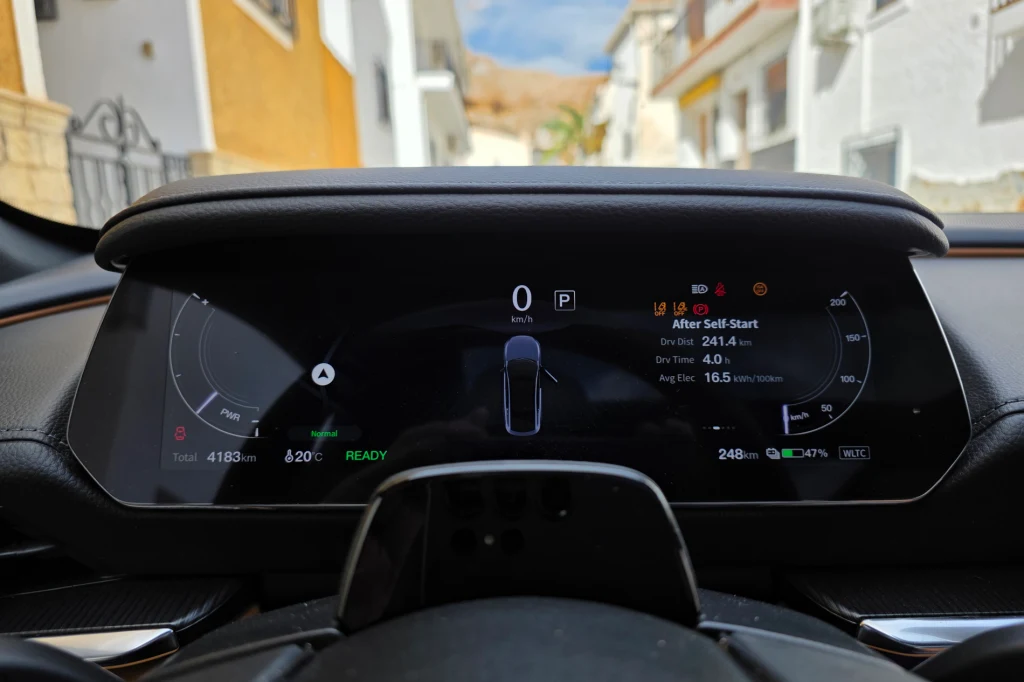 Cyfrowe wskaźniki przed kierowcą podają podstawowe informacje, wyświetlacz head-up jest seryjny, ale w testowym egzemplarzu nie pokazywał wskazań nawigacji Cyfrowy wyświetlacz deski rozdzielczej samochodu pokazujący podstawowe informacje dotyczące jazdy, takie jak prędkość, poziom naładowania baterii, zasięg oraz temperatura, z perspektywą zza kierownicy na ulicę miejską w tle.