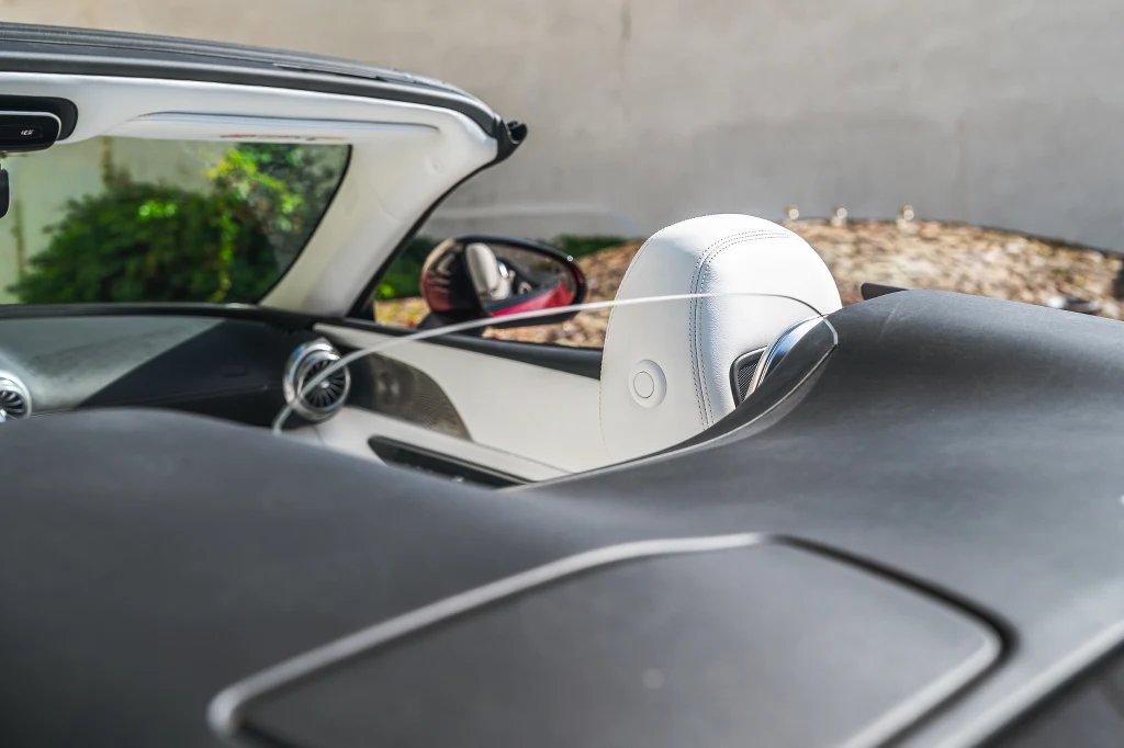 Wnętrze nowoczesnego kabrioletu z białą, skórzaną tapicerką foteli i efektownymi detalami, w tle widoczne boczne lusterko oraz fragment deski rozdzielczej.