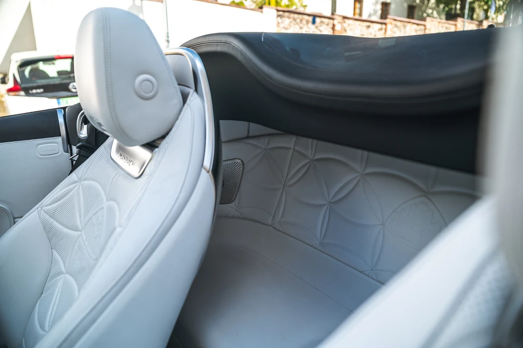 Luksusowe, jasne skórzane wnętrze samochodu kabrioleta z eleganckim wykończeniem, detale tapicerki z geometrycznym wzorem, widoczny zagłówek oraz fragment systemu audio.