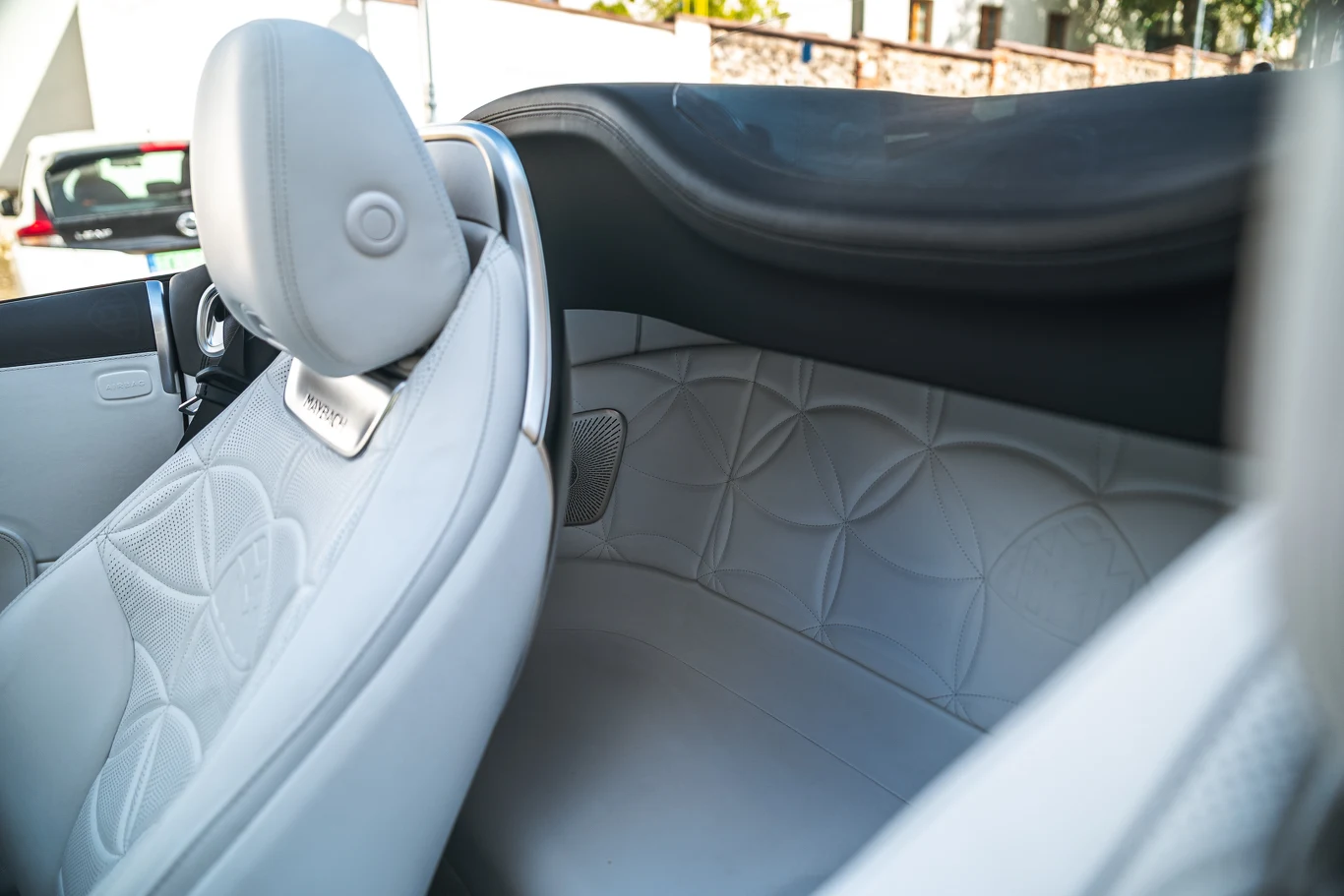 Luksusowe, jasne skórzane wnętrze samochodu kabrioleta z eleganckim wykończeniem, detale tapicerki z geometrycznym wzorem, widoczny zagłówek oraz fragment systemu audio.