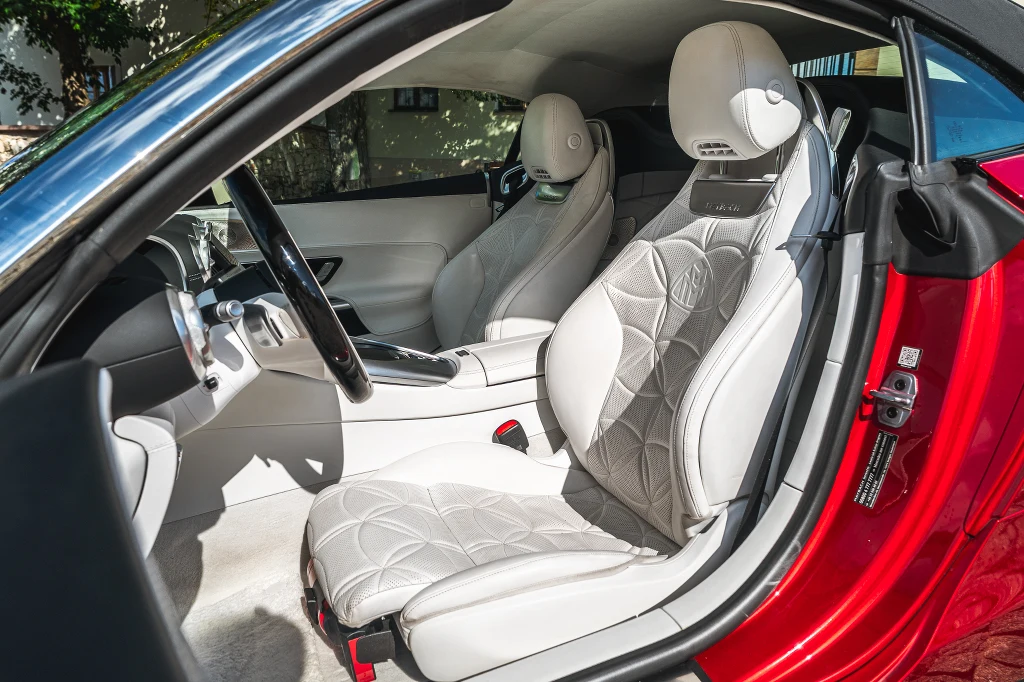 Luksusowe, jasne wnętrze nowoczesnego sportowego samochodu z charakterystycznie pikowanymi, skórzanymi fotelami, widoczna deska rozdzielcza, kierownica oraz fragment czerwonej karoserii.