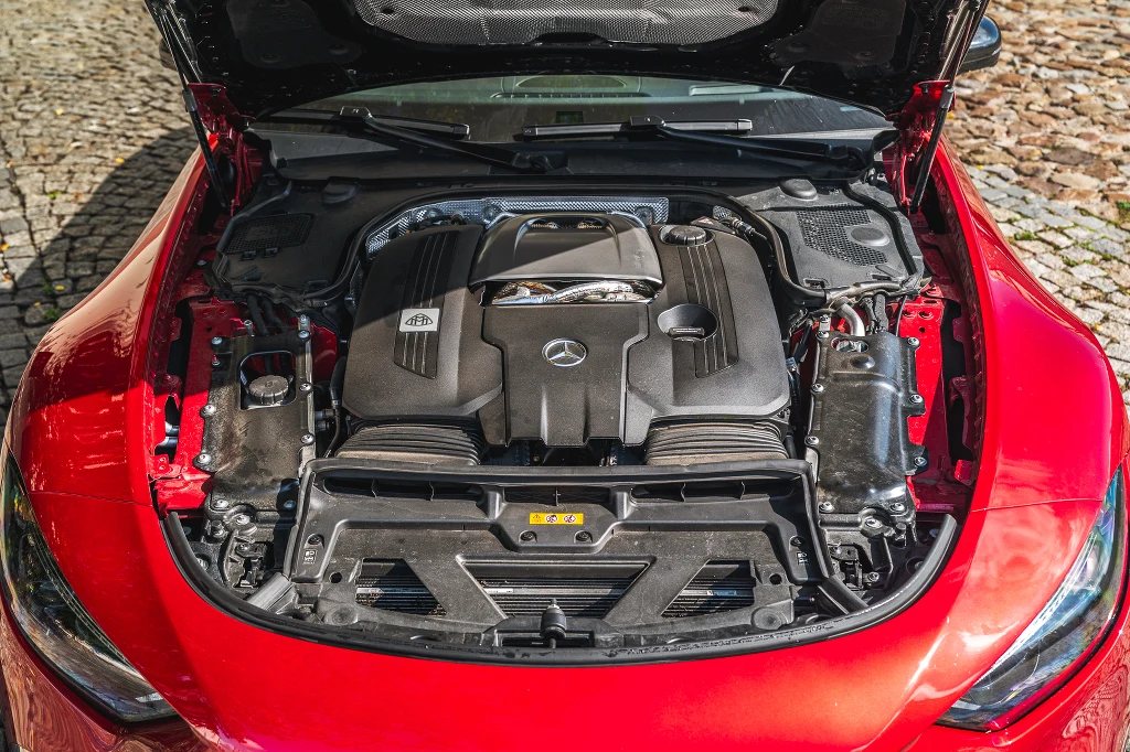 Silnik samochodowy marki Mercedes-Benz AMG zamontowany pod otwartą maską czerwonego auta, wyraźnie widoczne elementy mechaniczne i oznaczenia producenta.