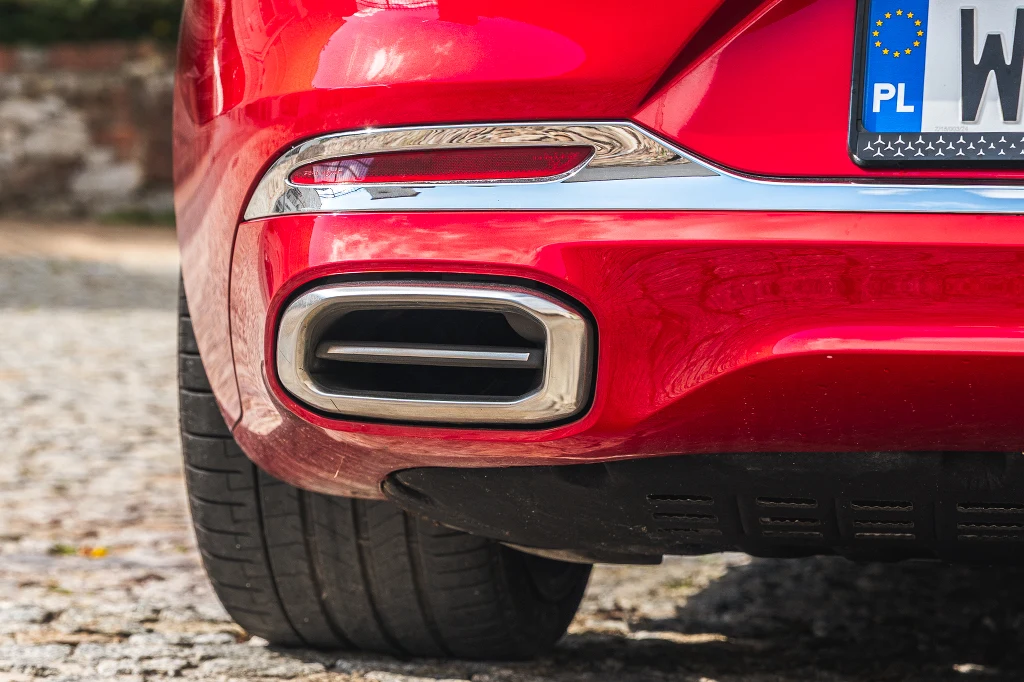 Czerwona karoseria samochodu, wyraźnie widoczny tylny zderzak, rura wydechowa w chromowanej oprawie oraz fragment polskiej tablicy rejestracyjnej.