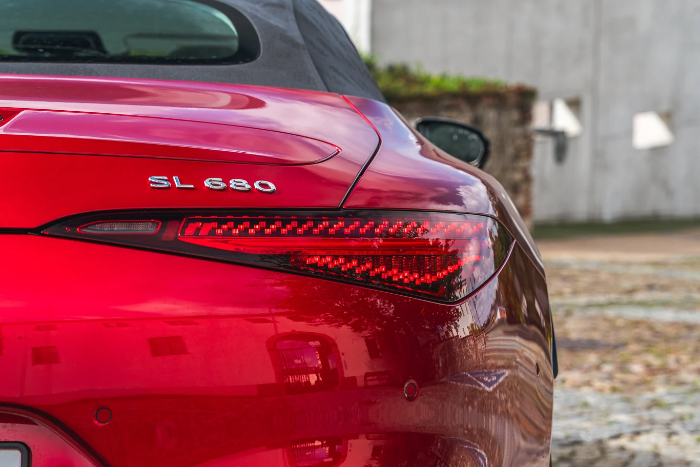 Czerwony samochód klasy premium, model Mercedes SL 680, ukazany z tyłu, wyraźnie widoczny nowoczesny tylny reflektor LED oraz oznaczenie modelu, w tle rozmyta ściana budynku.