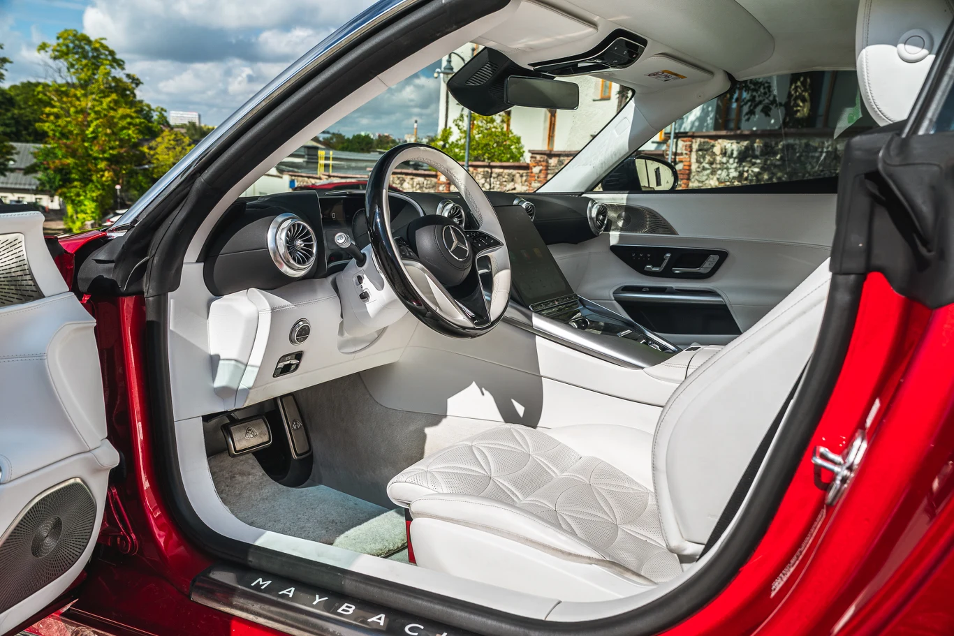 Luksusowe wnętrze samochodu z białą skórzaną tapicerką, nowoczesną deską rozdzielczą, sportową kierownicą i zaawansowanym panelem kontrolnym, podkreślone eleganckimi detalami i chromowanymi wykończeniami.