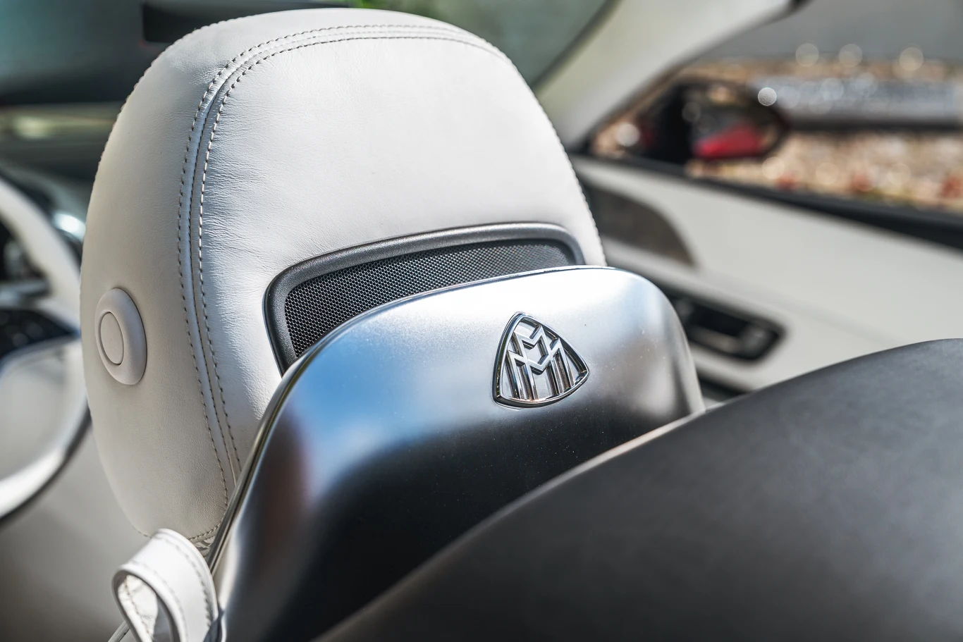 Jasna skórzana zagłówek samochodowy z wytłoczonym logo Maybach i elementem wykończeniowym z metalu, widoczny fragment wnętrza luksusowego auta.