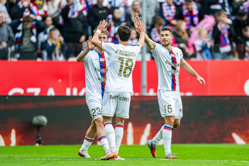 Kadr meczu Górnik Zabrze - Arka Gdynia Piłkarze drużyny świętują zdobycie gola na murawie stadionu, podnosząc ręce do wspólnego przybicia piątki. W tle widać trybuny z kibicami ubranymi w klubowe szaliki.