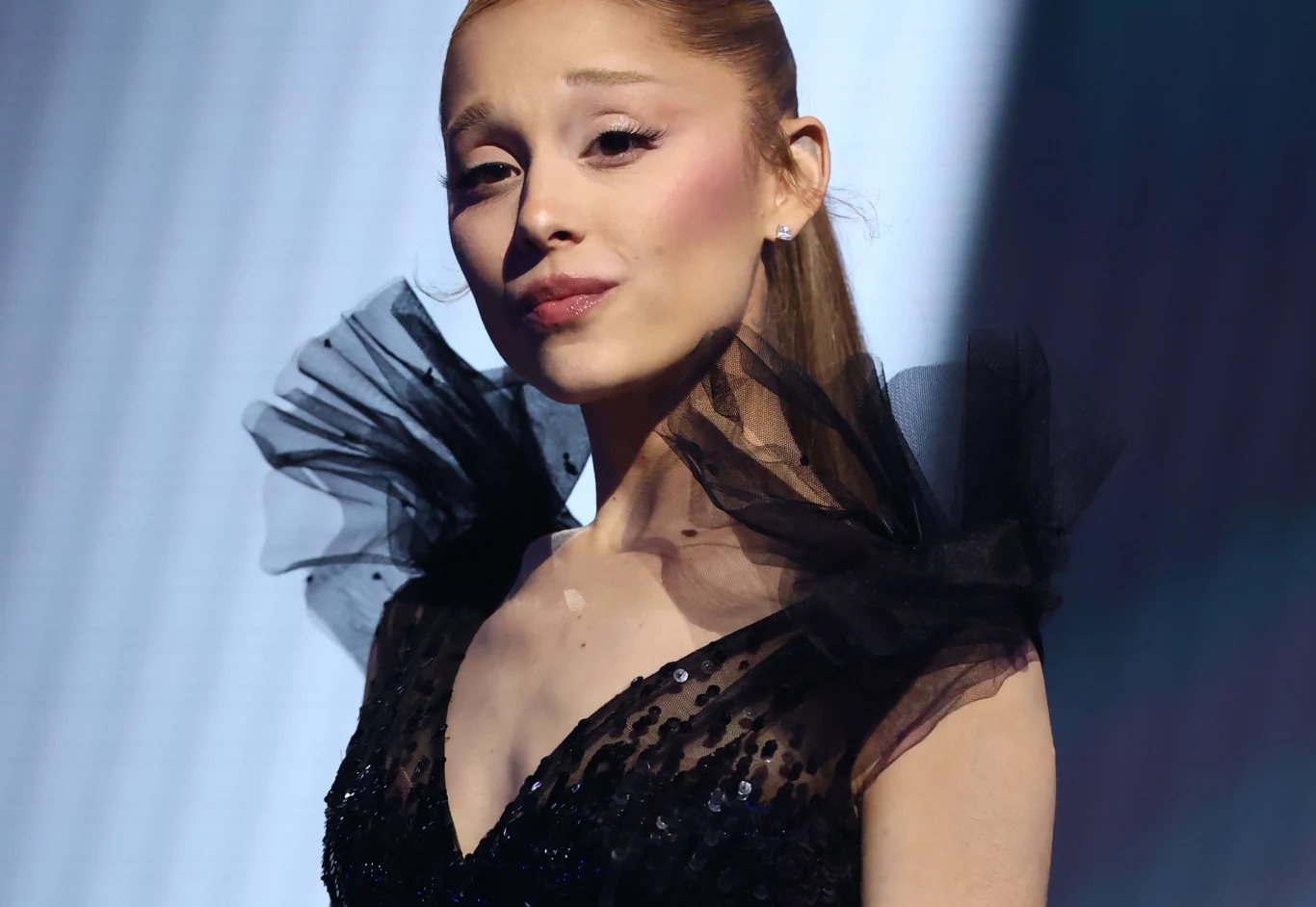 Ariana Gramde zagra w 13. sezonie "American Horror Story" Młoda kobieta w eleganckiej czarnej sukni z tiulowymi elementami na ramionach, spoglądająca na wprost, z delikatnym makijażem i upiętymi włosami.