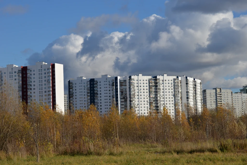 Na subit możemy trafić np. w bloku z PRL Wielokondygnacyjne bloki mieszkalne o jasnych elewacjach ustawione równolegle w tle, na pierwszym planie jesienne drzewa i trawy, po niebie przesuwają się duże, ciemne chmury.