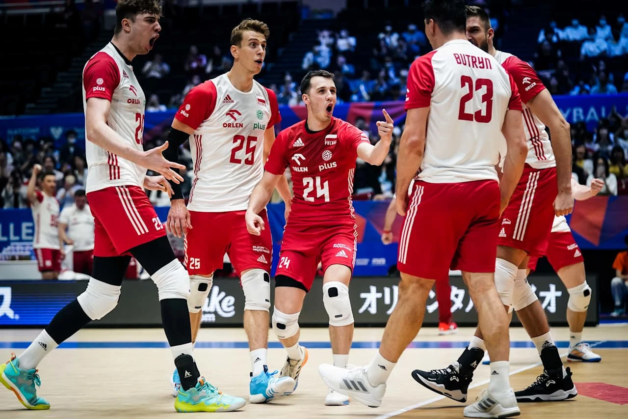 Grupa polskich siatkarzy w sportowych strojach na parkiecie podczas zaciętej wymiany, wyrażających silne emocje i zaangażowanie w grze, otoczona kibicami na hali.