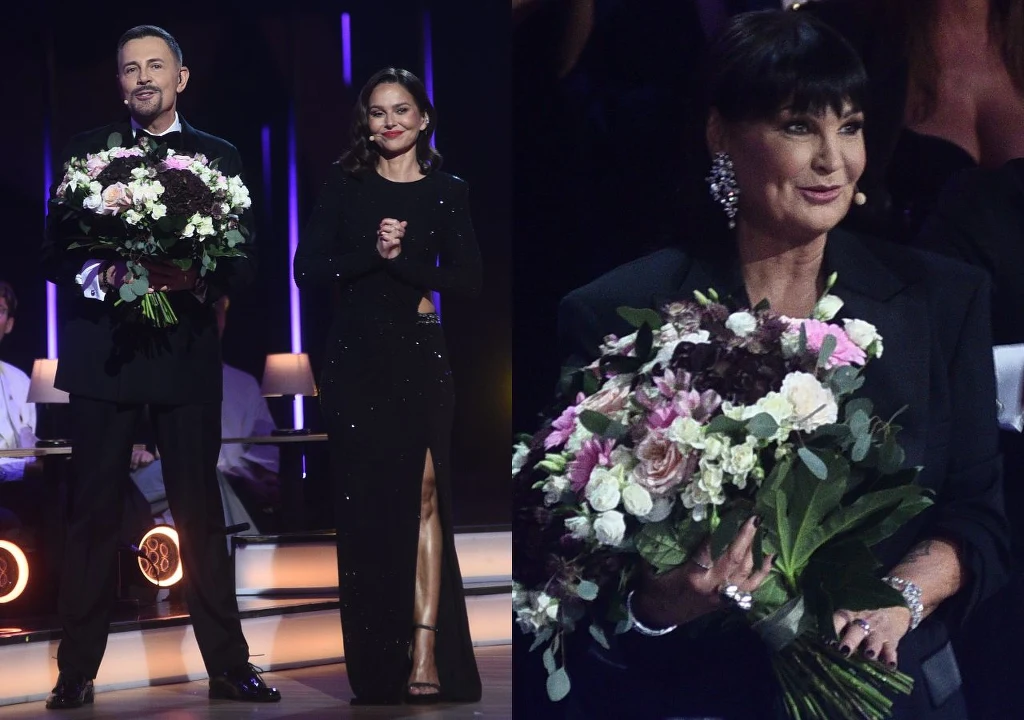 Trzy osoby ubrane elegancko, trzymające bukiety kwiatów, stoją na scenie podczas uroczystej gali lub programu telewizyjnego, w tle widoczne kolorowe oświetlenie.