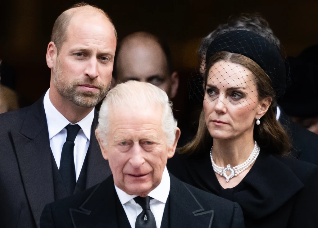 Trzy osoby w eleganckich, czarnych strojach żałobnych. Mężczyzna z przodu z siwymi włosami, mężczyzna z brodą i kobieta w perłowej biżuterii i woalce stoją za nim. Wszyscy mają poważne wyrazy twarzy.