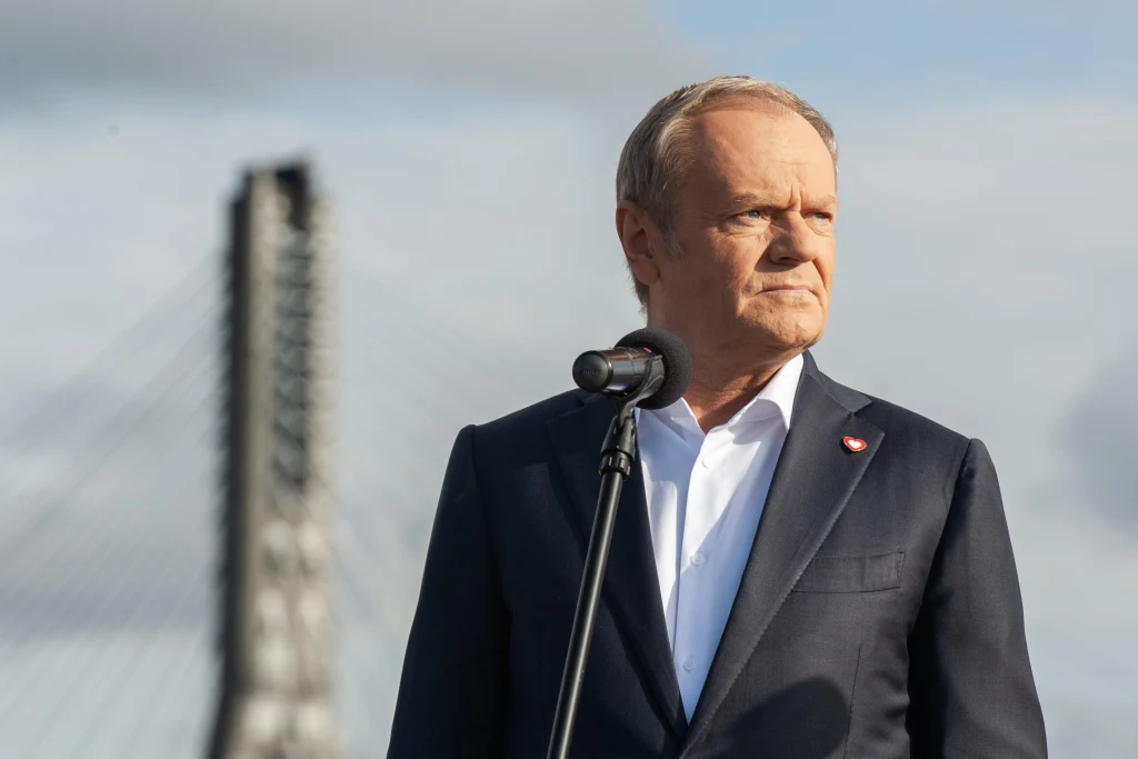 "Le Monde" pisze o impasie, w jakim znalazła się koalicja kierowana przez premiera Donalda Tuska Mężczyzna w jasnej koszuli i ciemnej marynarce stoi przy mikrofonie na tle mostu o wyraźnych linach nośnych i nieba z chmurami. Na jego klapie widoczna przypinka w kształcie serca.