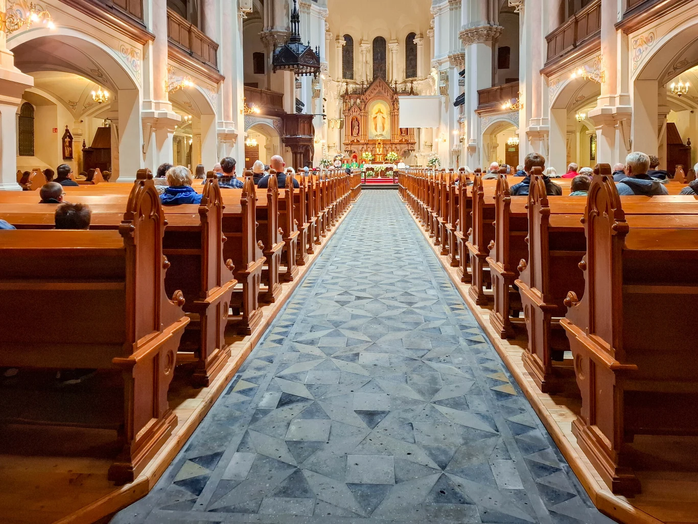 1 stycznia trzeba iść do kościoła? Wytyczne są jasne Wnętrze przestronnej świątyni z wysokimi filarami oraz bogato zdobionym ołtarzem, w ławkach siedzą wierni, skupieni podczas nabożeństwa; centralną część prowadzi szeroki chodnik wyłożony dekoracyjnymi płytkami.