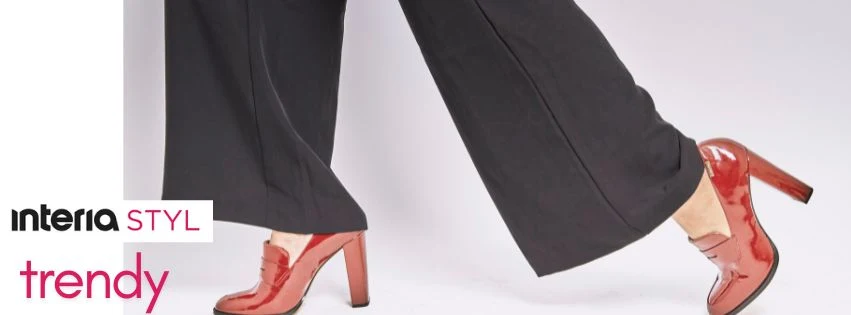 Trendy zmieniają się co chwilę, ale to ty decydujesz, które do ciebie pasują Czerwone lakierowane buty na wysokim obcasie na nogach osoby w czarnych, szerokich spodniach, białe tło, elementy graficzne z napisem 'interia STYL trendy'.