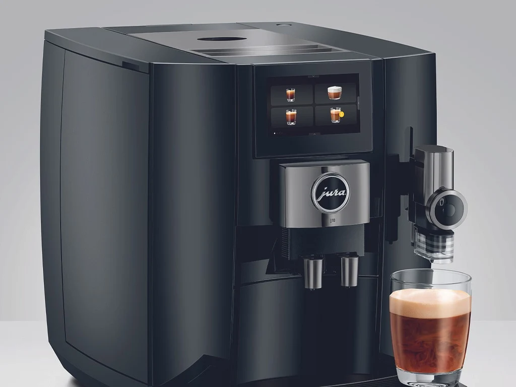 Ekspres JURA J10. Źródło: Oficjalne zdjęcie producenta Czarny ekspres do kawy marki Jura z nowoczesnym panelem dotykowym oraz filiżanką kawy z pianką ustawioną z przodu urządzenia.