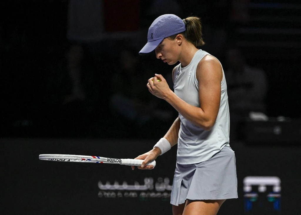 Iga Świątek Tenisistka w jasnej sportowej sukience i czapce z daszkiem świętuje zdobyty punkt, trzymając rakietę tenisową i zaciśniętą pięść, stojąc na korcie podczas rozgrywki.