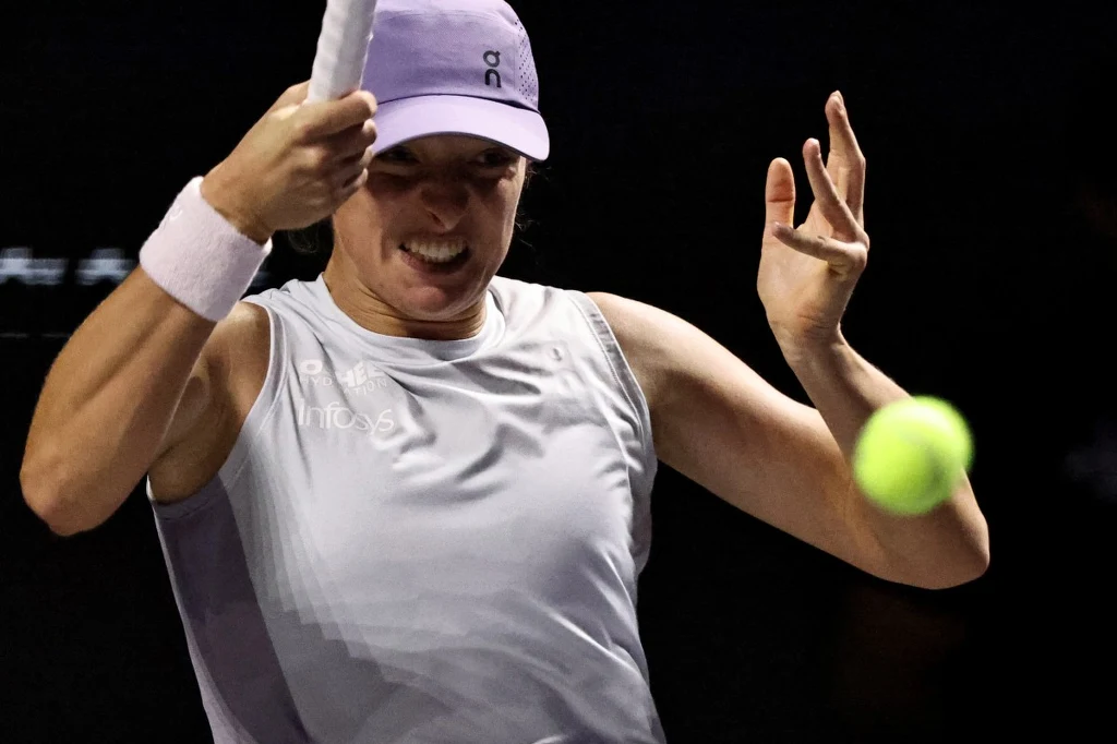 Znamy godzinę meczu Świątek - Anisimova w Rijadzie Tenisistka w fioletowej koszulce i czapce wykonuje dynamiczne uderzenie, skupiona na zbliżającej się piłce tenisowej, na ciemnym tle kortu wewnętrznego.