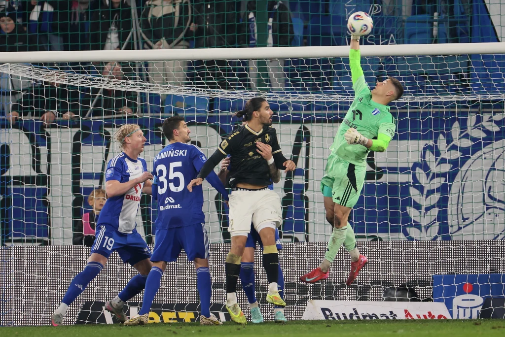 Pogoń próbowała działań odwetowych, ale Rafał Leszczyński spisywał się w bramce "Nafciarzy" be zarzutu Bramkarz w zielonym stroju wybija piłkę ponad poprzeczką bramki, a kilku zawodników drużyn w niebieskich i ciemnych strojach walczy o pozycję w polu karnym podczas meczu piłki nożnej.