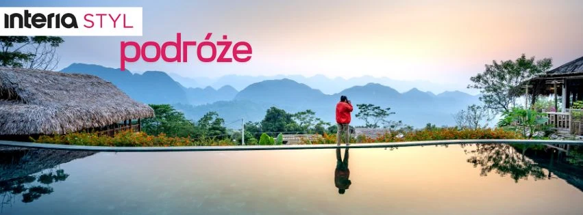 Podróżnik z czerwonym plecakiem stoi przy krawędzi basenu, podziwiając widok na górskie pasma pokryte mgłą w trakcie wschodu lub zachodu słońca, otoczony egzotyczną roślinnością i zabudowaniami w stylu tropikalnym.