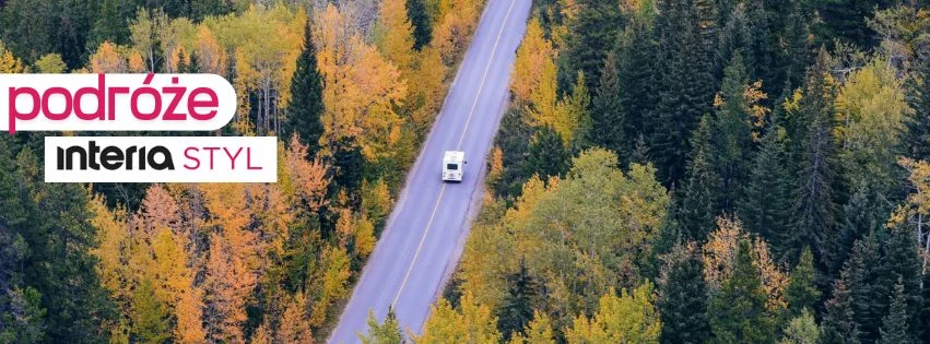 Zainspiruj się miejscami, które zachwycają krajobrazem, kulturą i lokalnymi zwyczajami Samotny kamper jedzie asfaltową drogą otoczoną gęstym lasem w jesiennych kolorach, przewaga żółci i zieleni podkreśla klimat spokojnej, przyrodniczej scenerii.
