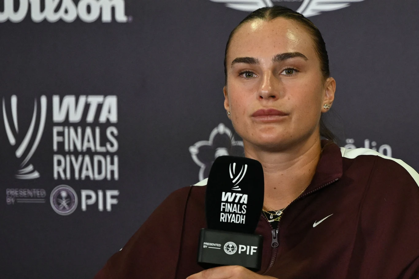 Aryna Sabalenka podczas WTA Finals 2025 Kobieta w sportowej kurtce trzyma mikrofon z logo PIF, w tle widoczne napisy WTA Finals Riyadh, logo turnieju i sponsorów.