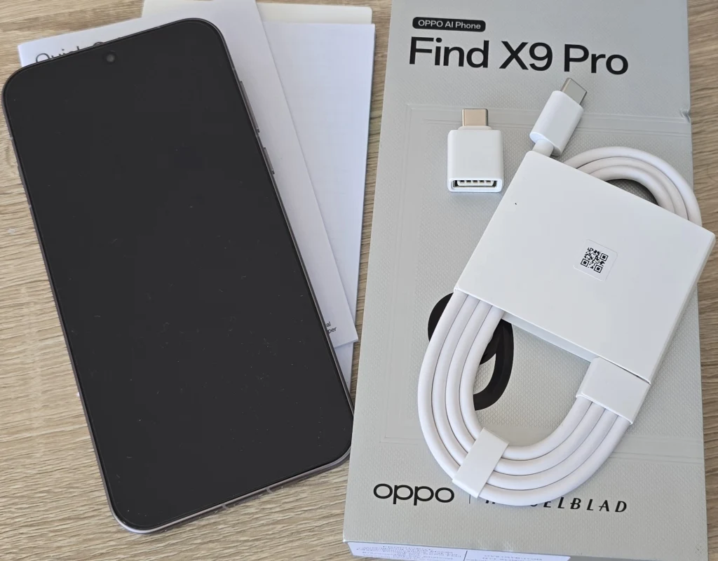 Unboxing Oppo Find X9 Pro. Co mamy w pudełku? Smartfon z czarnym ekranem po lewej stronie, obok pudełko z napisem Find X9 Pro oraz białe akcesoria: kabel USB-C, adapter i dokumentacja. Wszystko leży na drewnianym blacie.