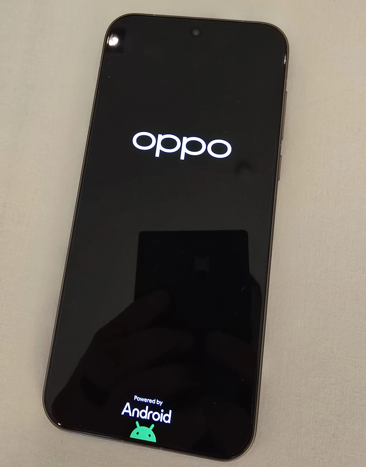 Pierwsze uruchomienie. 3600 nitów wyświetlacza gwarantuje dobrą czytelność nawet w pełnym słońcu. Smartfon marki Oppo z ekranem startowym, na którym widoczne jest logo producenta oraz napis Powered by Android wraz z symbolem systemu. Telefon leży na jasnej powierzchni, widać subtelne odbicie osoby trzymającej aparat.