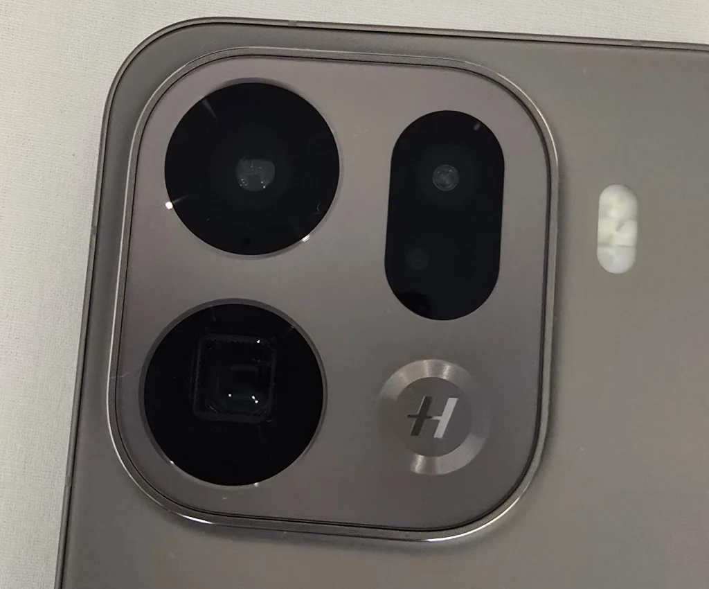 W Oppo Find X9 Pro wyspa z aparatami jest prostokątna. Zbliżenie na moduł aparatów fotograficznych w smartfonie, trzy wyraźnie widoczne obiektywy oraz lampa błyskowa na srebrnej, metalicznej obudowie, z wyraźnym oznaczeniem producenta przy jednym z obiektywów.