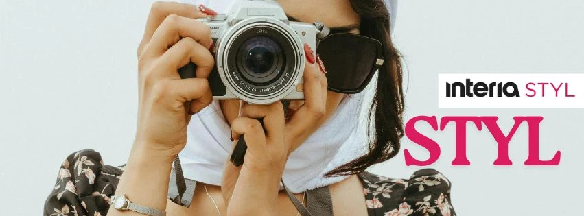 Kobieta z białym nakryciem głowy i okularami przeciwsłonecznymi trzyma aparat fotograficzny, skierowany w stronę obiektywu. W tle widoczny napis 'STYL' oraz logo 'interia STYL'.