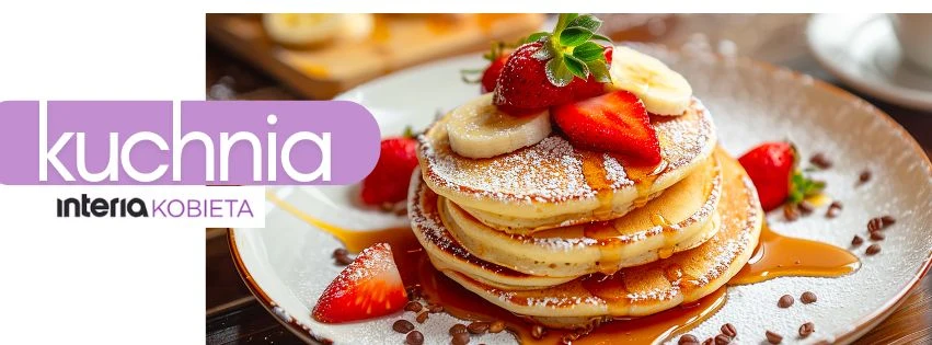 Stos naleśników polanych syropem klonowym, posypanych cukrem pudrem, ozdobionych plasterkami banana i świeżymi truskawkami, podany na talerzu, wokół rozsypane kawałki czekolady.