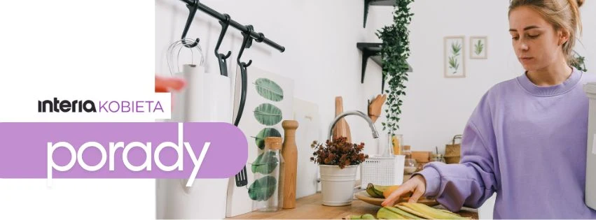 Sprzątanie nigdy nie było prostsze i przyjemniejsze Kobieta w jasnofioletowej bluzie przygotowuje jedzenie w domowej, nowoczesnej kuchni ozdobionej zielonymi motywami roślinnymi. Na blacie leżą warzywa, a w tle widoczne są kuchenne akcesoria i dekoracje.